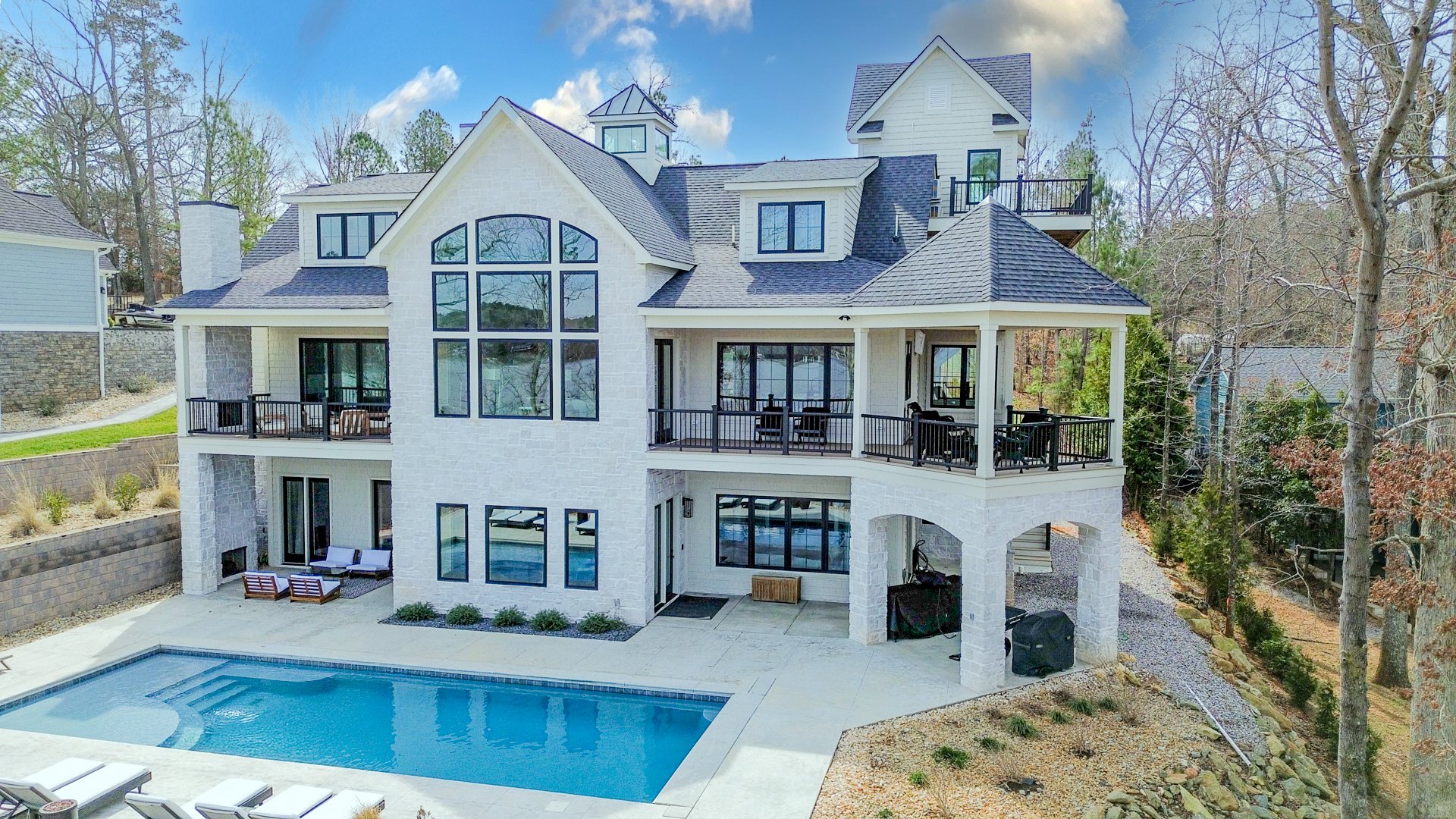 White stone lake house with arched windows, decks, and a pool